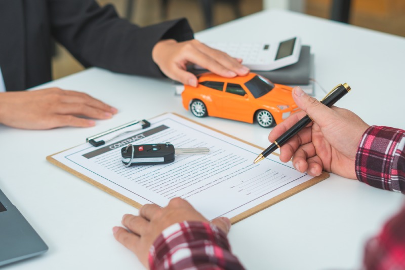 Man signing car insurance document or lease paper. Writing signature on contract or agreement. Buying or selling new or used vehicle. Car keys on table. Warranty or guarantee. Customer or salesman.