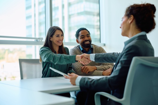 Happy multiracial couple came to agreement with insurance agent during a meeting in the office. Women are shaking hands. Copy space.