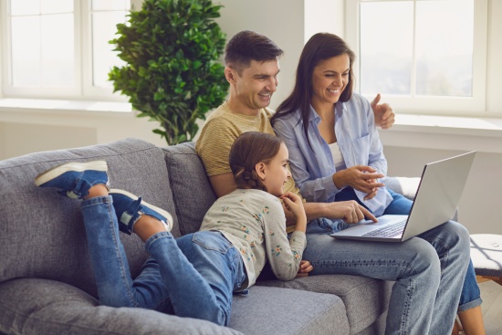 Happy family looking at a laptop while sitting comfortably on a sofa in a living room at the weekend.