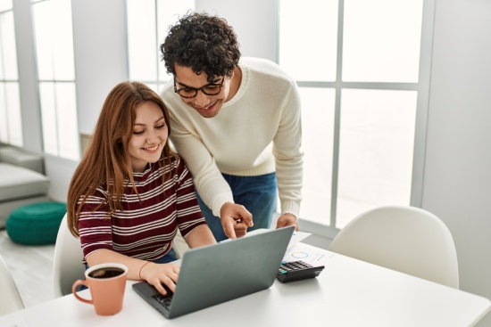 Young couple using laptop and drinking coffee sitting on the table at home.