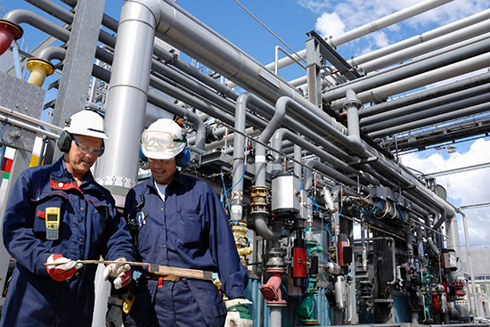 Oil workers talking, wearing safety equipment. Oil plant.